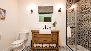 Un baño con inodoro, lavamanos, tocador de madera y zona de ducha.
