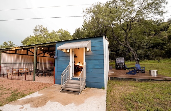 A small blue building with a covered outdoor seating area and a staircase leading to the entrance. - Gorgeous Tiny House with Fire Pit, Games and Barbecue in San Saba, Texas (San Saba)