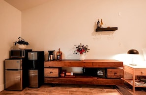 A kitchenette with a microwave, coffee maker, and refrigerator. There is a wooden shelf with a vase of flowers and a bottle on it. - Gorgeous Tiny House with Fire Pit, Games and Barbecue in San Saba, Texas (San Saba)