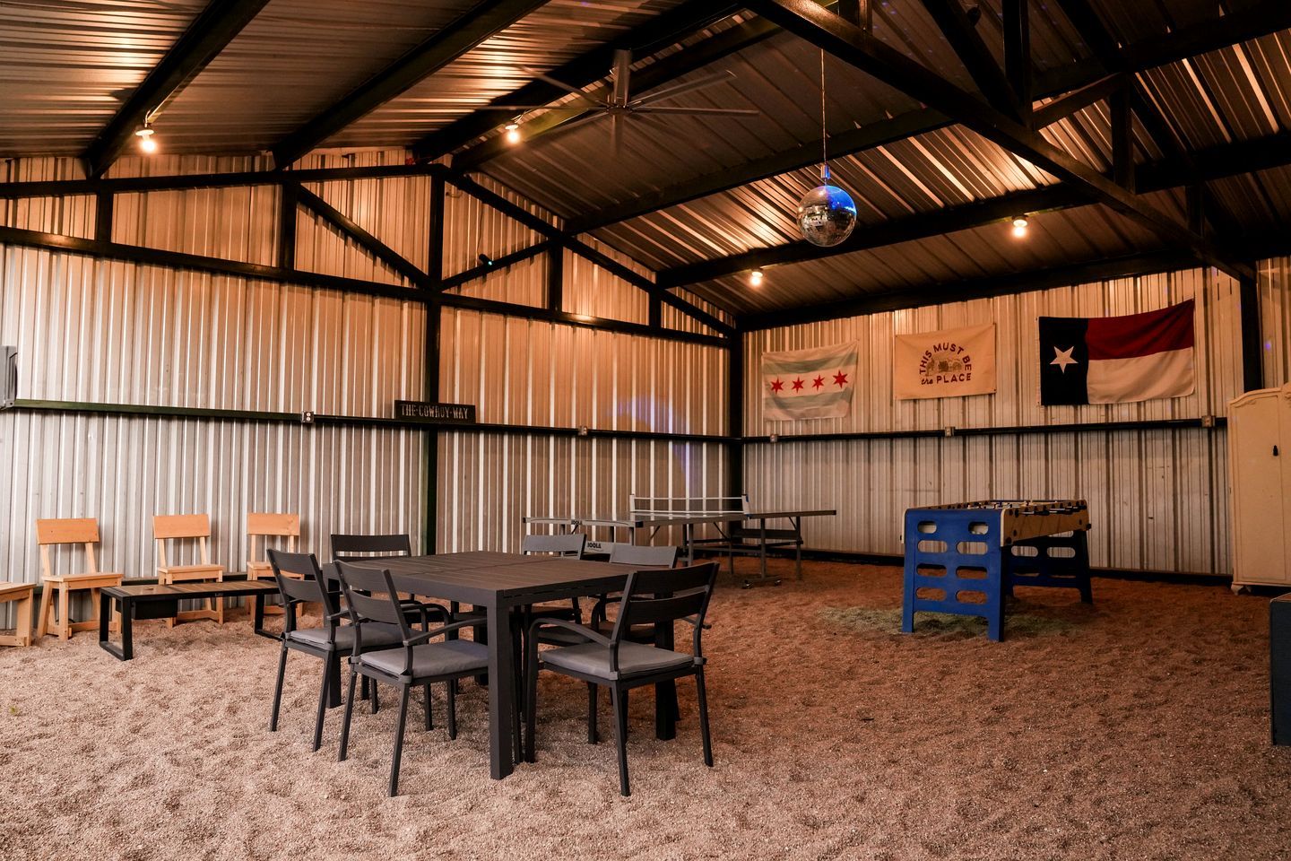 A spacious indoor area with a high ceiling, metal walls, and a table with chairs. There are flags and a sign on the walls.