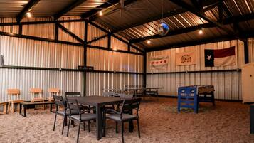 A spacious indoor area with a high ceiling, metal walls, and a table with chairs. There are flags and a sign on the walls.