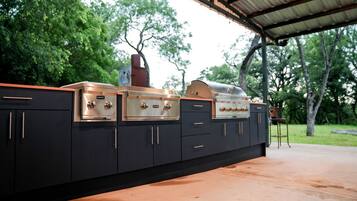 A black outdoor kitchen with two built-in grills and a barbecue smoker, set against a backdrop of trees.