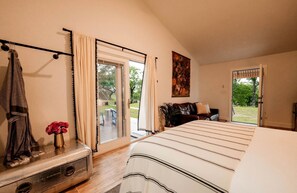 A bedroom with a bed, a sliding glass door to a patio, a coat rack, and a painting on the wall. - Gorgeous Tiny House with Fire Pit, Games and Barbecue in San Saba, Texas (San Saba)
