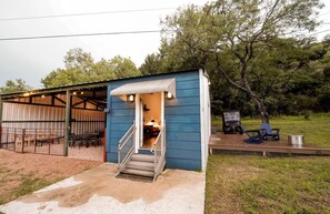 A small blue building with a covered outdoor seating area and a staircase leading to the entrance. - Gorgeous Tiny House with Fire Pit, Games and Barbecue in San Saba, Texas (San Saba)