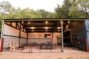 A covered outdoor area with a metal roof, a fenced enclosure, and a flag. - Gorgeous Tiny House with Fire Pit, Games and Barbecue in San Saba, Texas (San Saba)