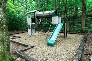 Un parque infantil con tobogán y estructura de escalada, rodeado de árboles.