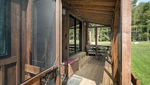 A wooden deck with a bench, a table, and a view of a grassy area. - Scandinavian-Style Cottage Fully Equipped in Vermont (Wolcott)