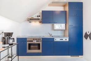 A modern kitchen with blue cabinets, a built-in oven, a microwave, and a coffee maker.