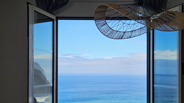 A room with a large window offering a view of the ocean. - Roof 360! (Boaventura)
