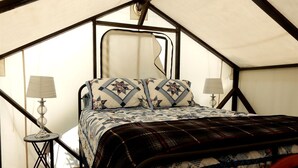 Ein Zelttraum mit Bett, zwei Lampen und Holzboden.