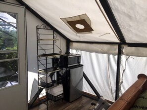 Una habitación compacta con kitchenette, una estantería metálica y una ventana.