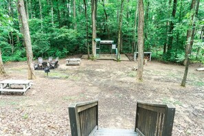 Un terrain de camping boisé, équipé de tables de pique-nique, de chaises et d’un abri.
