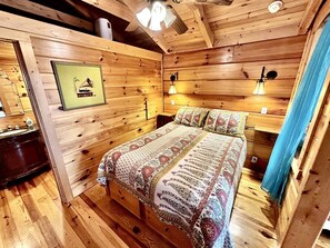 Une pièce aménagée comme un chalet en bois, avec un lit, des lampes de chevet et un tableau encadré au mur.