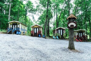 Une rangée de cabanes, avec un chemin de gravier menant à elles, le tout entouré d’arbres.