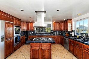 A modern kitchen with wooden cabinets, a central island, and a large window offering a view. - Secluded Cabin with Breathtaking Lake Views and Foosball Table in Big Bear Lake, California (Big Bear Lake)
