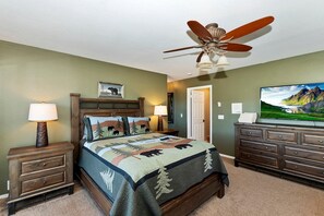 Quarto com cama, ventoinha no teto, televisão e cômoda.