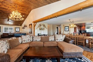 A spacious living room with a large sectional sofa, a wooden coffee table, and a chandelier. - Secluded Cabin with Breathtaking Lake Views and Foosball Table in Big Bear Lake, California (Big Bear Lake)