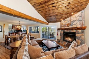 A spacious living room with a stone fireplace, wooden ceiling beams, and a large sofa. - Secluded Cabin with Breathtaking Lake Views and Foosball Table in Big Bear Lake, California (Big Bear Lake)
