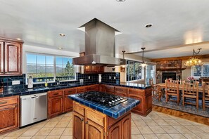 A kitchen with a central island, wooden cabinets, a stove, and a stone fireplace. - Secluded Cabin with Breathtaking Lake Views and Foosball Table in Big Bear Lake, California (Big Bear Lake)