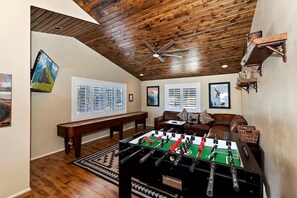 Quarto com mesa de futebol, sofá e ventilador de teto.