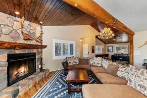 A cozy living room with a stone fireplace, a large sofa set, a wooden coffee table, and a chandelier. - Secluded Cabin with Breathtaking Lake Views and Foosball Table in Big Bear Lake, California (Big Bear Lake)