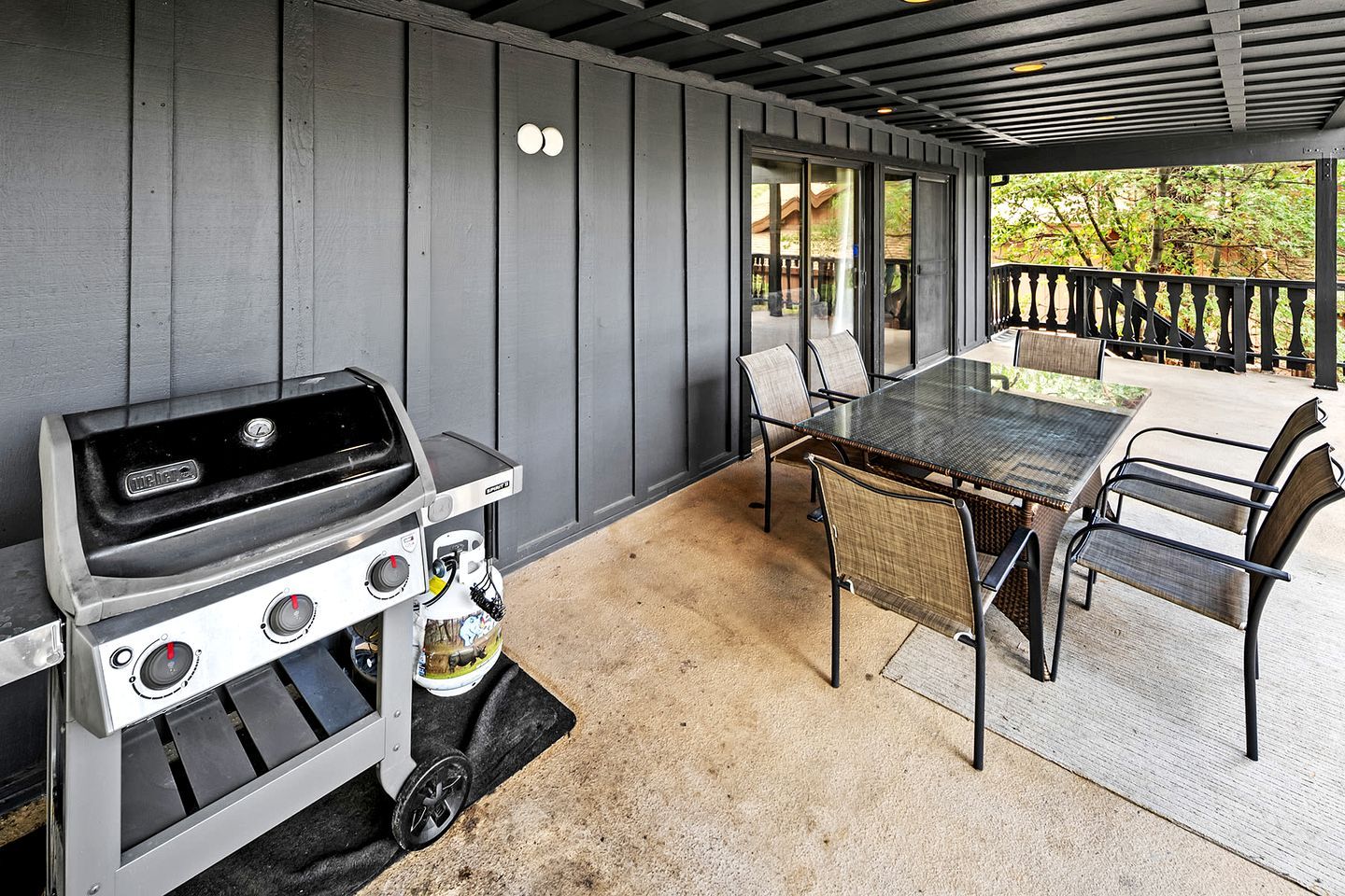 A covered outdoor area with a grill, a table, and chairs.