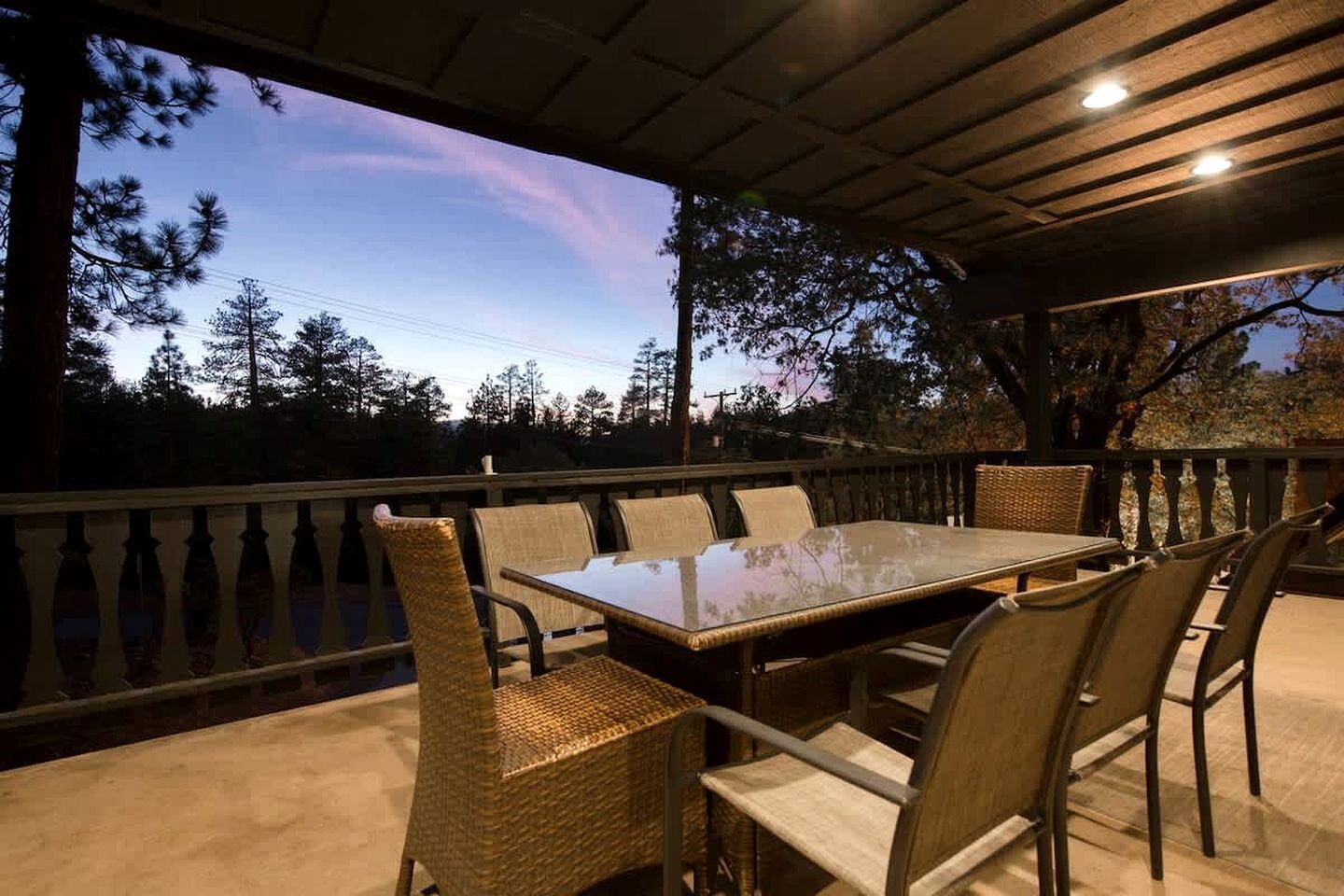Une terrasse extérieure dotée d’une table à plateau de verre et de chaises en osier, le tout entouré d’une balustrade en bois.