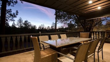 Une terrasse extérieure dotée d’une table à plateau de verre et de chaises en osier, le tout entouré d’une balustrade en bois.