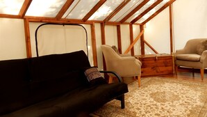 A room with a sloped ceiling, wooden beams, a black sofa, a beige armchair, and a patterned rug.
