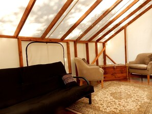 A room with a sloped ceiling, wooden beams, a black sofa, a beige armchair, and a patterned rug.