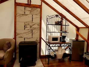 Acogedor dormitorio en ático con chimenea, un sofá, una estantería metálica con electrodomésticos y techo de madera.