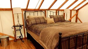 Ein Schlafzimmer mit Holzboden, einem Metallbettgestell, gemusterten Betttextilien, einem kleinen Tisch mit Lampe und einem Mülleimer.