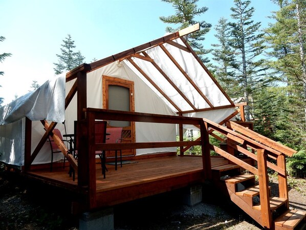 A wooden cabin with a covered deck, a chair, and a window.