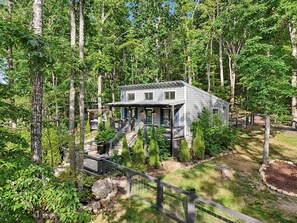 A house surrounded by trees, with a porch and a staircase leading to the entrance. - Exquisite Cabin with Stunning Interior, Outdoor Deck and Hot-Tub in Tennessee (Tracy City)