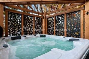 A hot tub in a wooden gazebo with a decorative black and gold panel backdrop. - Exquisite Cabin with Stunning Interior, Outdoor Deck and Hot-Tub in Tennessee (Tracy City)
