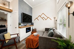 A modern living room with a flat-screen TV, a fireplace, a sofa, and a dining area. - Exquisite Cabin with Stunning Interior, Outdoor Deck and Hot-Tub in Tennessee (Tracy City)