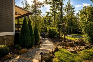 A pathway leading to a wooden deck with a seating area, surrounded by a landscaped garden with various shrubs and a stone wall. - Exquisite Cabin with Stunning Interior, Outdoor Deck and Hot-Tub in Tennessee (Tracy City)
