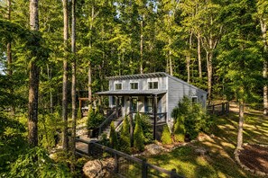 A modern cabin surrounded by a forest with a deck and stairs leading to the entrance. - Exquisite Cabin with Stunning Interior, Outdoor Deck and Hot-Tub in Tennessee (Tracy City)