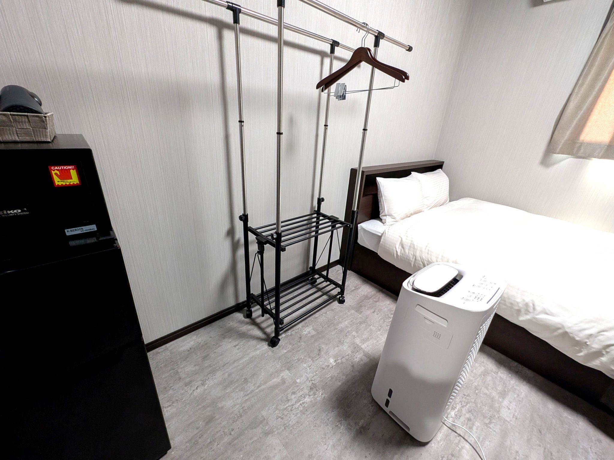 A hotel room with a bed, a black drying rack, and a white appliance, possibly a dryer.