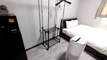 A hotel room with a bed, a black drying rack, and a white appliance, possibly a dryer.
