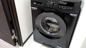 A black front-loading washing machine with a control panel, a basket on top, and a door with a latch. - AMISTADHOTEL  ANNEXE (Matsuura)
