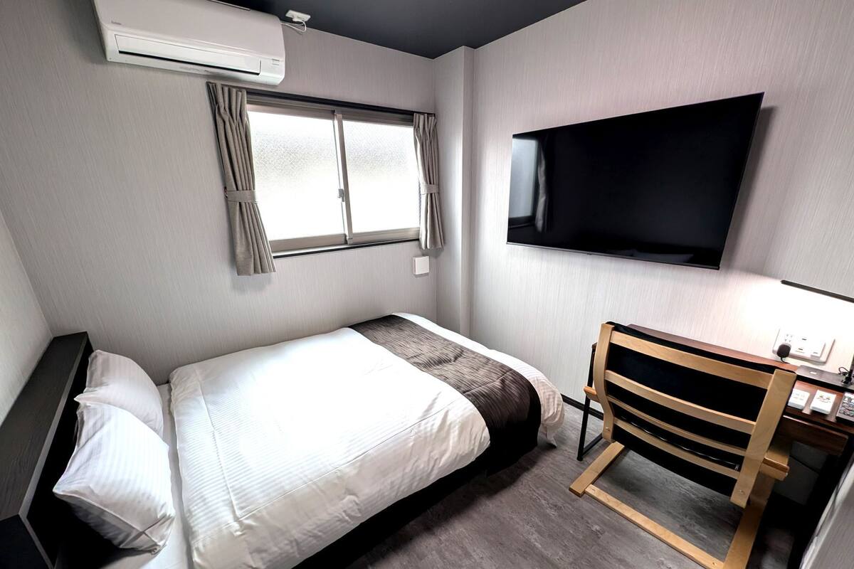 A hotel room with a bed, a desk, a chair, a TV, and a window.