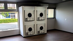 A laundry room with four stacked washing machines, large windows with a view of the street, and a wooden floor. - AMISTADHOTEL  ANNEXE (Matsuura)