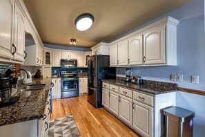 A kitchen with white cabinets, granite countertops, a black refrigerator, an oven, a microwave, and a coffee maker. - Amazing Lakefront Cabin Perfect for Groups in Topton, North Carolina (Topton)