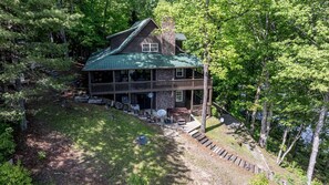 Une cabane avec un toit végétalisé, une cheminée en pierre et une véranda dotée de sièges d’extérieur.