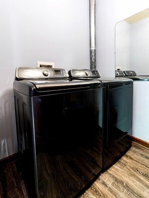 A laundry room with two front-loading washers and dryers, a wooden floor, and a white wall. - Amazing Lakefront Cabin Perfect for Groups in Topton, North Carolina (Topton)