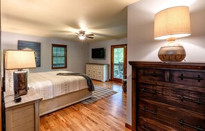Une chambre à coucher avec un lit, une commode, une lampe, un ventilateur de plafond et un téléviseur fixé au mur.