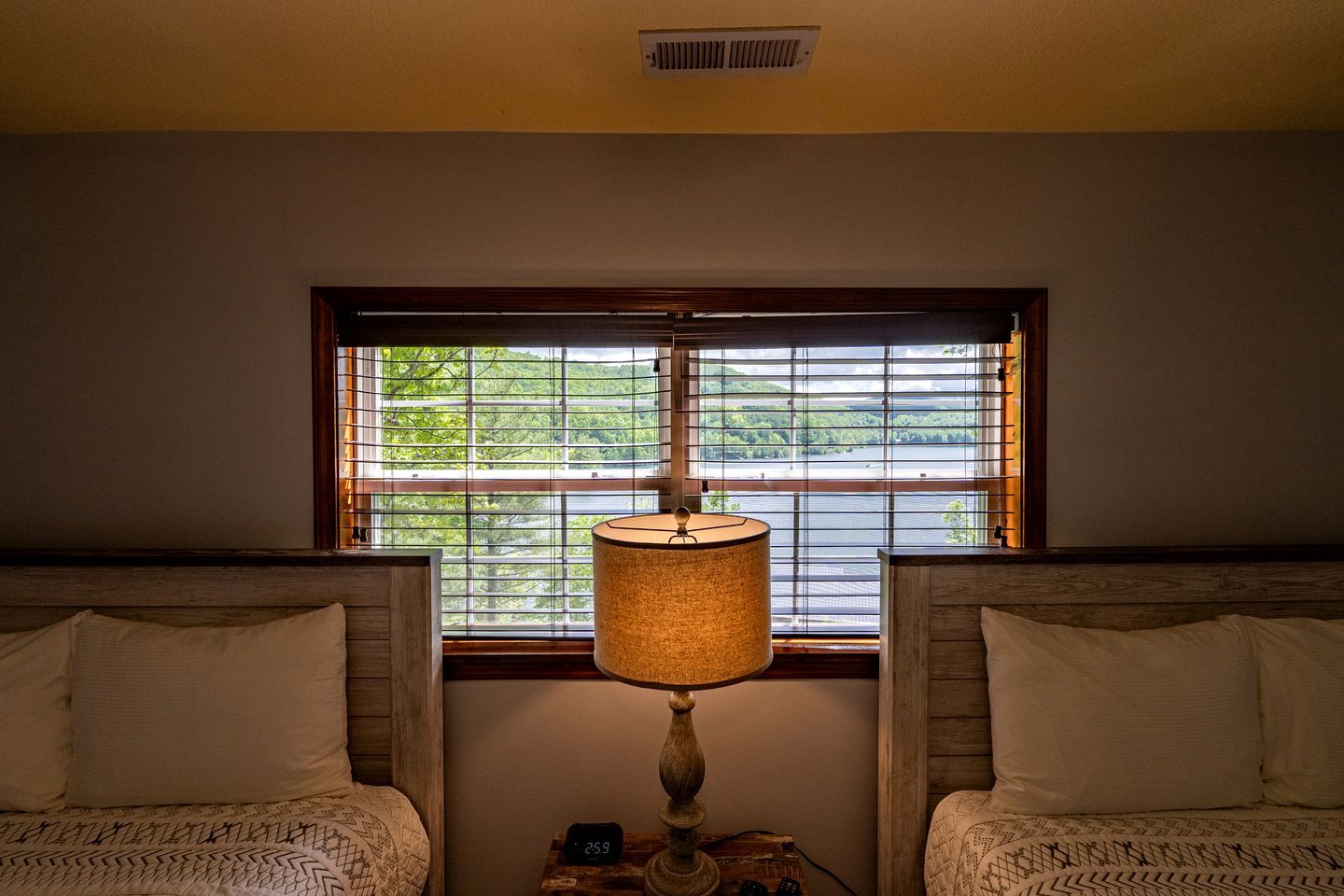 A bedroom with two beds, a window with blinds, a lamp, and a clock.