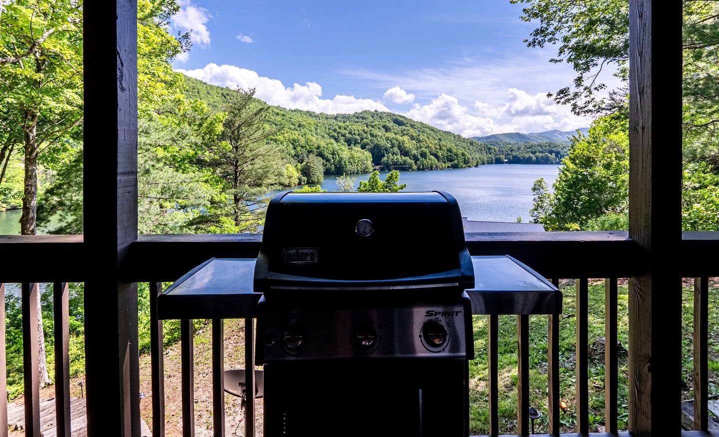 Ein Grill auf einer Holterrasse mit Blick auf einen See und Wald.