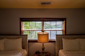 Une chambre avec deux lits, une fenêtre avec des stores, une lampe et une horloge.